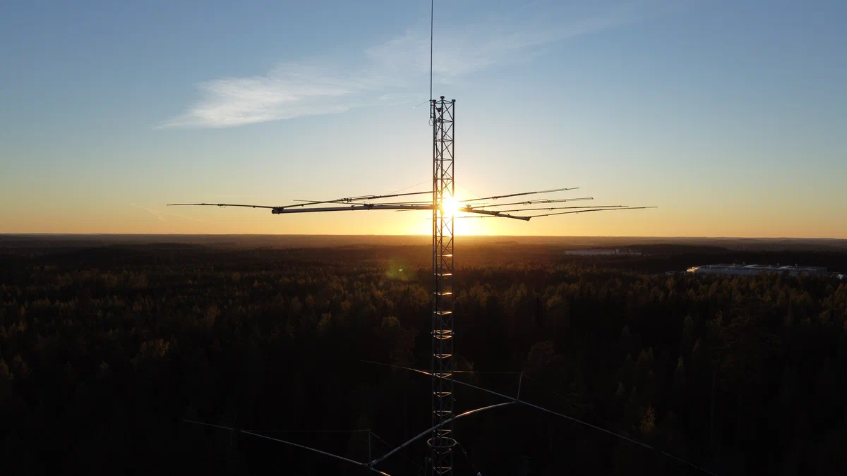 A Yagi antenna on a lattice tower against an autumn sunset, above a forest
