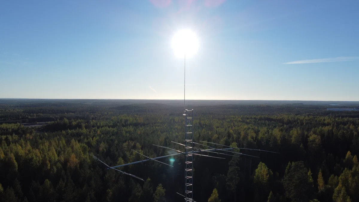 The top of a club station's lattice tower from above, the summer sun over the forest
