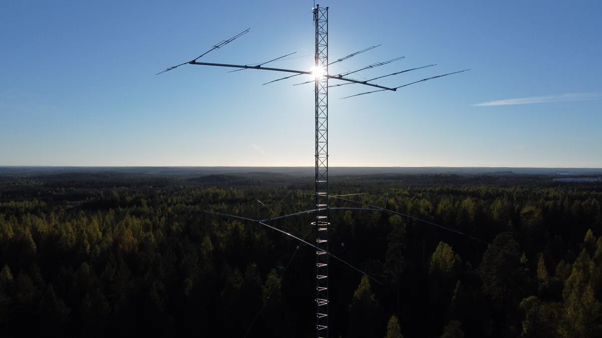 A Yagi antenna on a lattice tower against the summer sun, above a forest
