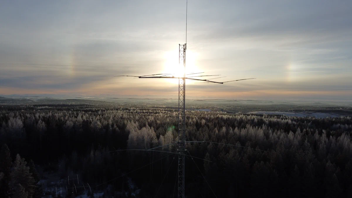 A Yagi antenna on a tower against the winter sun, with sun dogs, above a frosty forest
